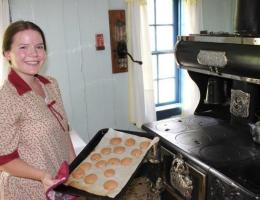 An interpreter in 1920s costume pulls a tray of cookies out of a wood-burning oven