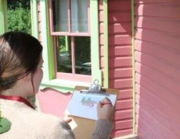An interpreter in 1920s costume paints a picture on the Stephansson House porch
