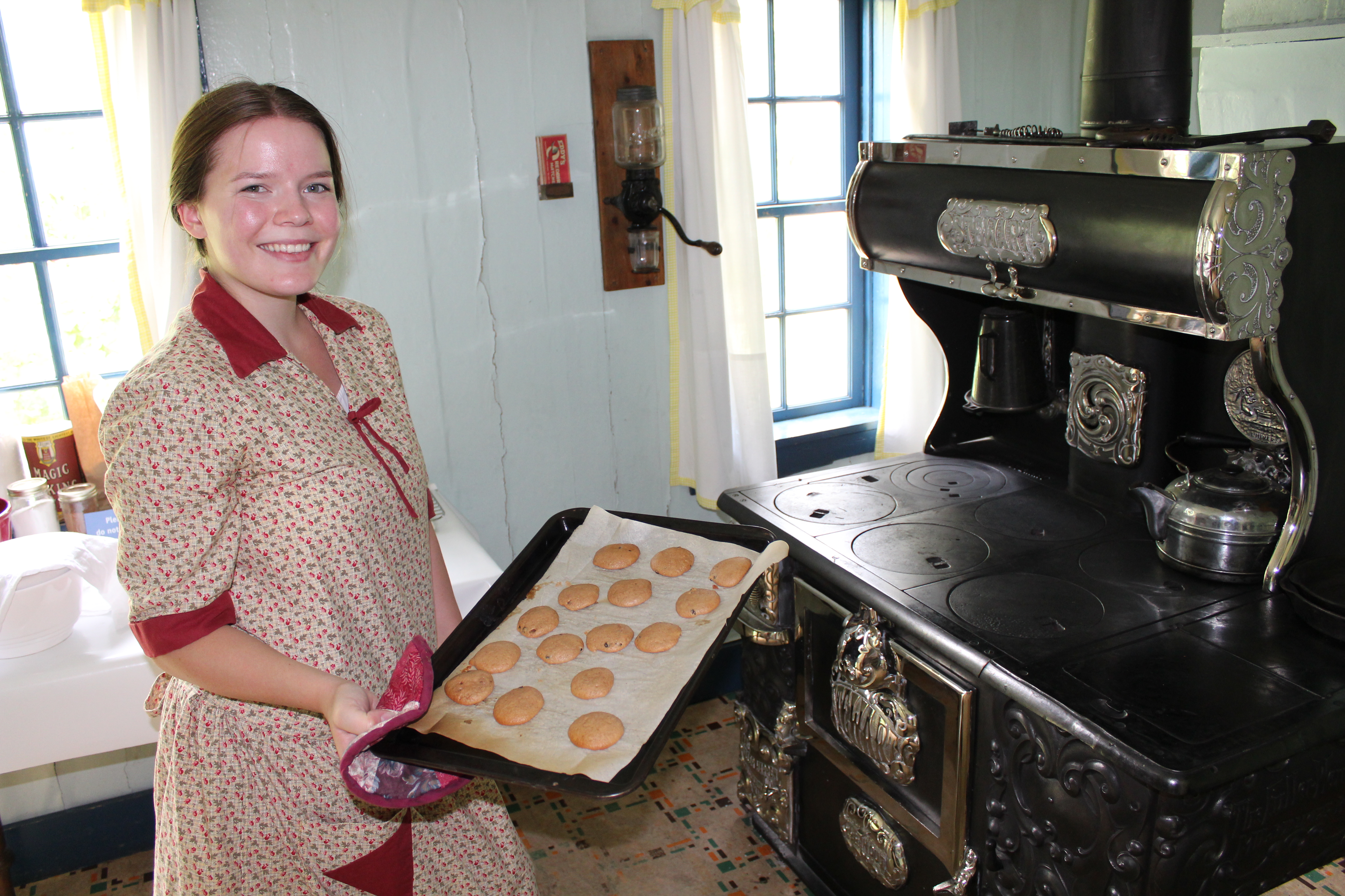 A staff member in 1920s costume takes a tray of cookies out of an old-fashioned wood-burning oven.